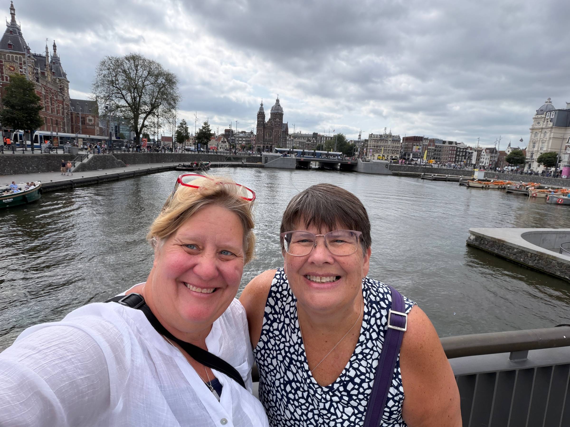 Two women in front of a canal in Amsterdam with houses in the background