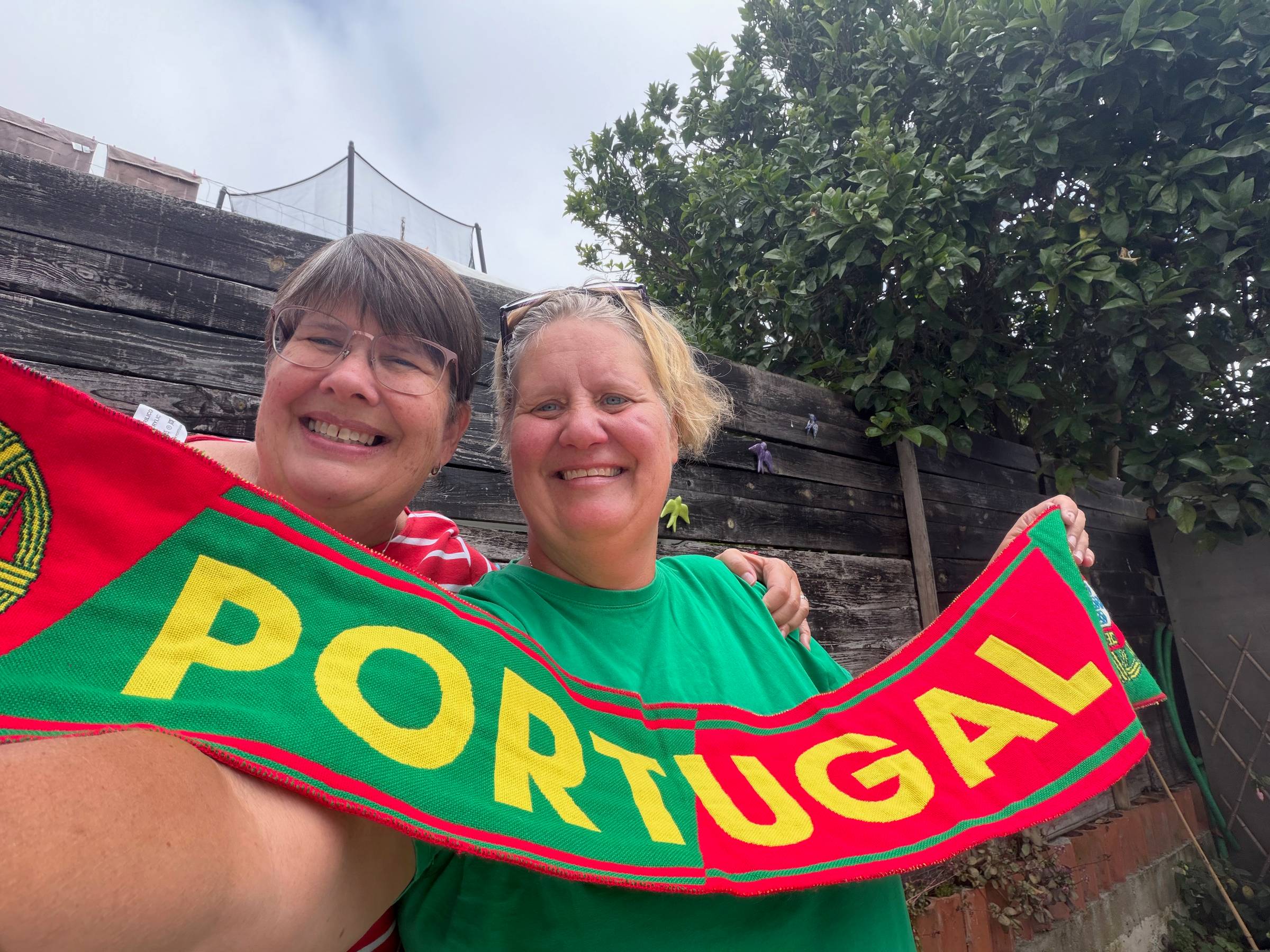 Two women holding a green and red scarf with the word Portugal in gold across it 
