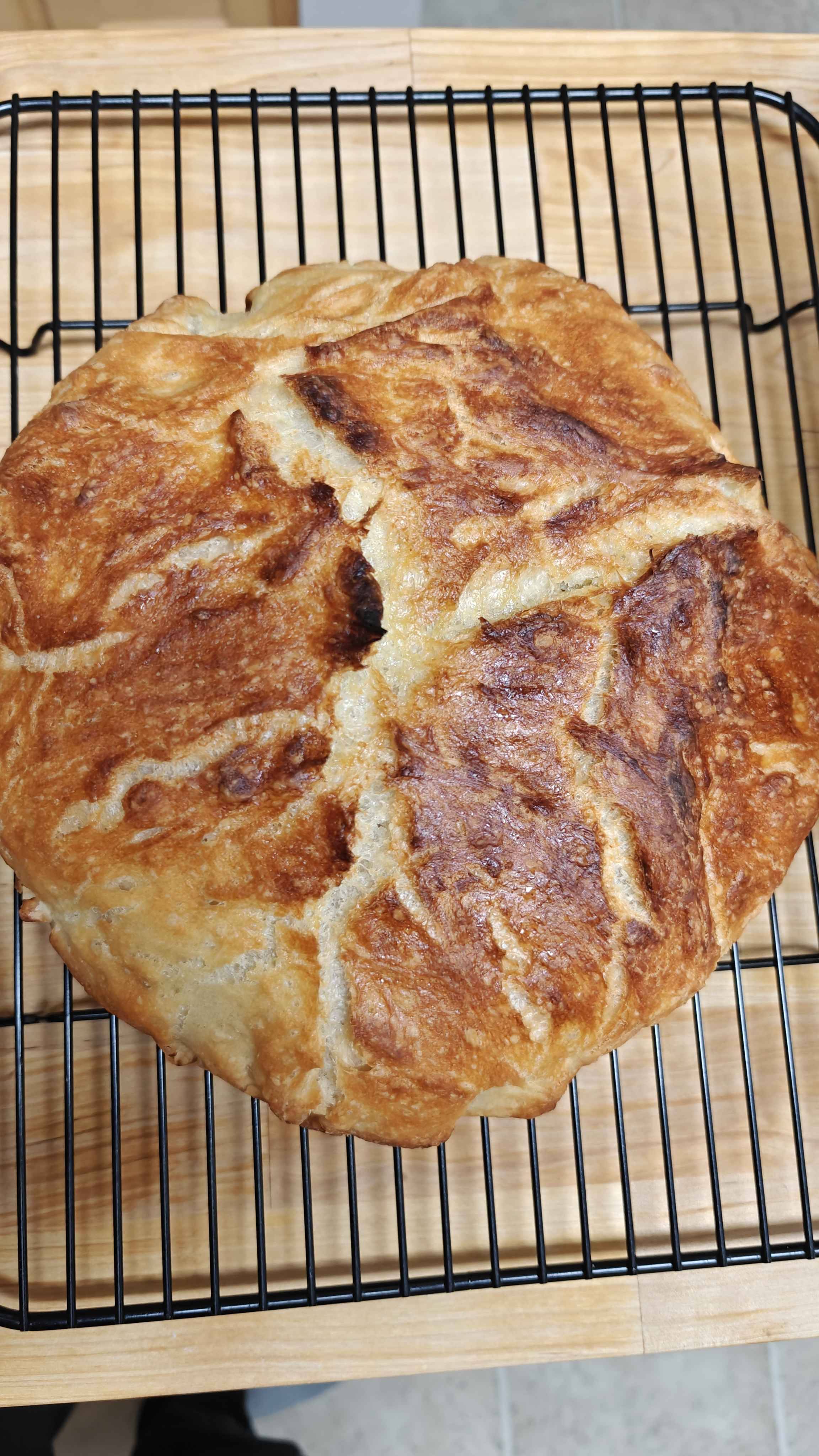 a loaf of bread on a black wire rack. It has a golden crust that almost looks like a dry riverbed but in a good way lol