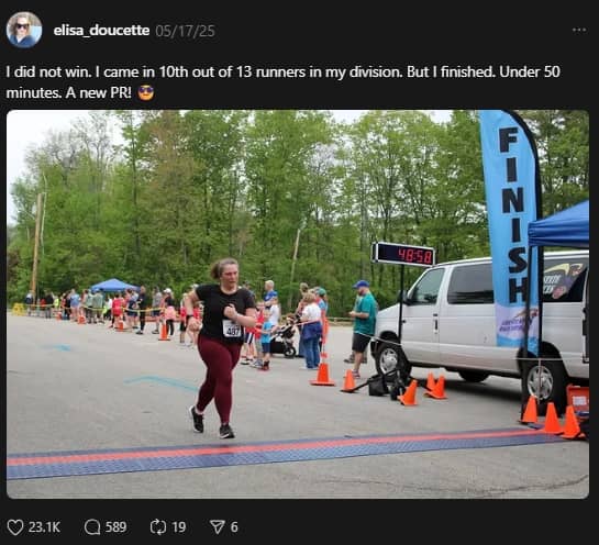 A screenshot of a social media post from user @elisa_doucette showing a woman running across the finish line of a 5K race. The digital clock reads 48:58, and spectators stand behind cones near a “FINISH” banner. The caption reads: “I did not win. I came in 10th out of 13 runners in my division. But I finished. Under 50 minutes. A new PR!”