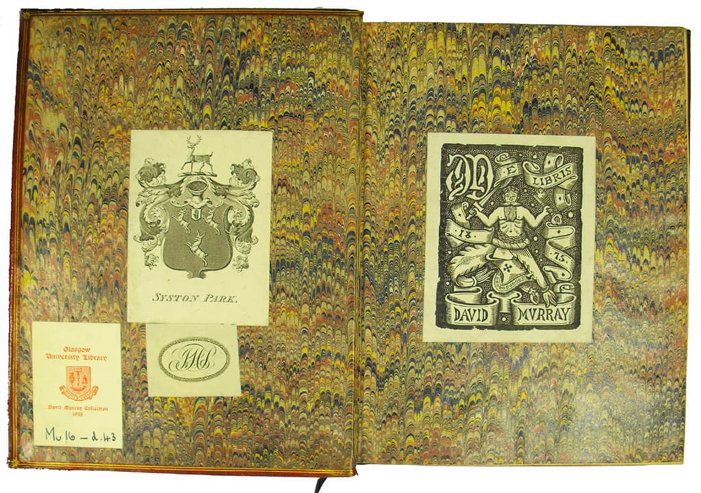 Open book with marbled endpapers displaying four vintage bookplates. On the left page: an ornate heraldic crest labeled "Syston Park," a circular monogram with the initials "MB," a bookplate from the Glasgow University Library, and a handwritten call numb