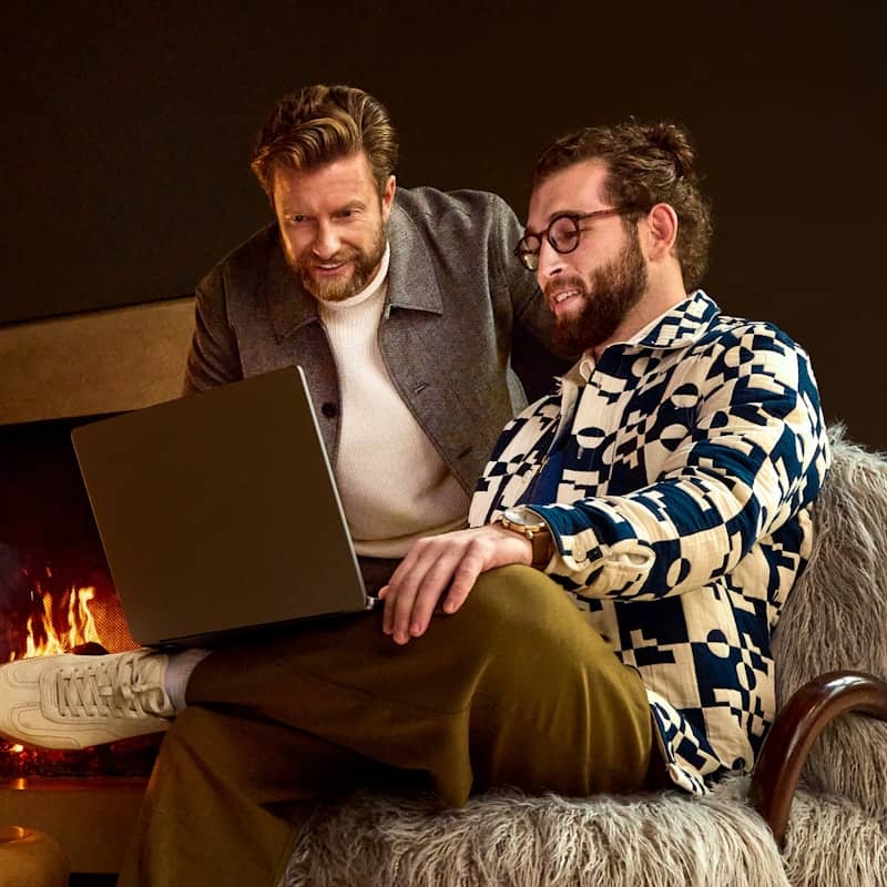 Two men looking at a laptop near a fireplace