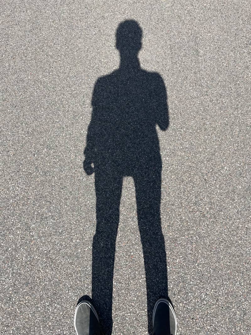 Shadow of a person standing on asphalt ground.