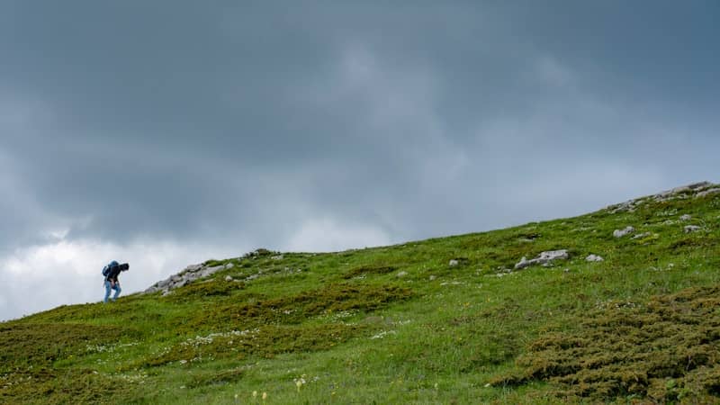 Hiker with backpack on grassy mountain under cloudy sky