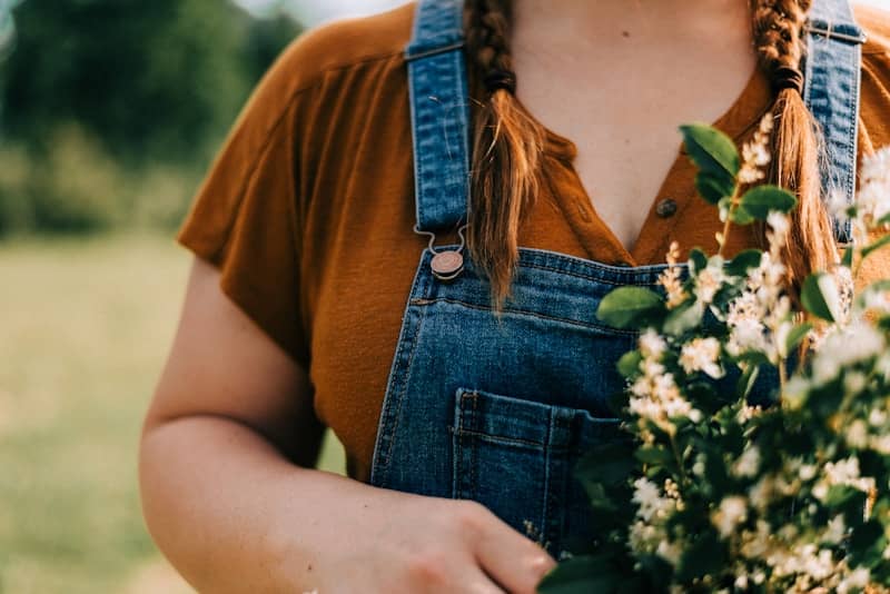 woman in brown crew neck t-shirt and blue denim dungaree holding white flowers