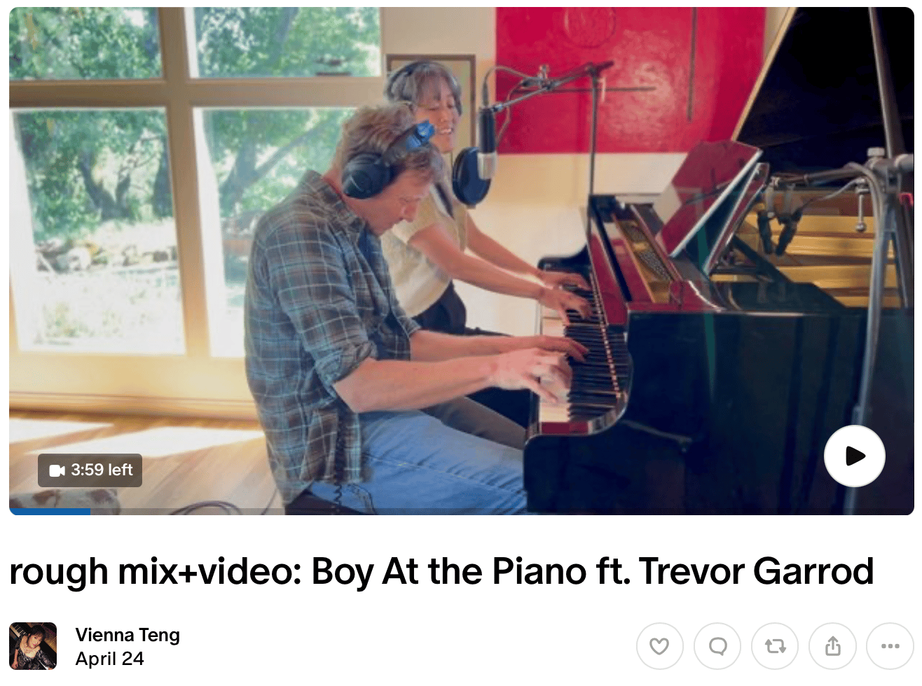 Screenshot of Vienna's Patreon post "rough mix+video: Boy At the Piano ft. Trevor Garrod." Vienna plays the lower half of the piano and sings into a microphone, wearing a short-sleeve bolero sweater and black headphones, and Trevor plays the upper half of the piano, shoulders hunched and wearing a green plaid work shirt and jeans, along with similar black headphones. A large window behind them looks out on trees and grass, and a large red square painting is on the wall behind Vienna. Two microphones pointed at the strings of the grand piano are visible as well.