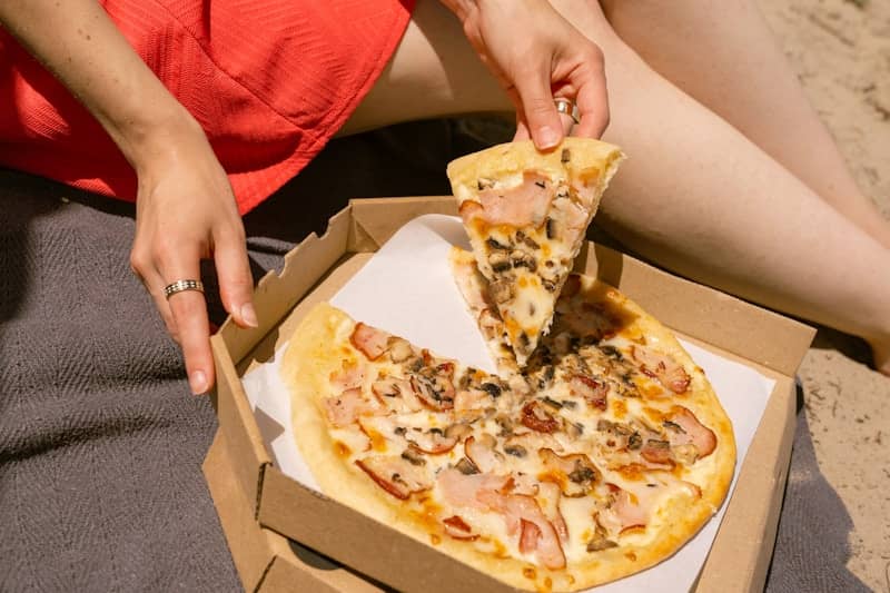 Woman's hand taking a pizza slice from a box.