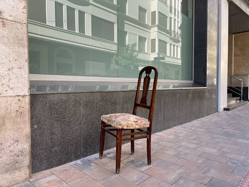 Vintage wooden chair with upholstered seat on a city sidewalk.