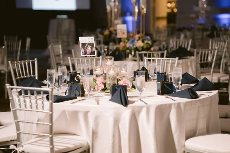 Event table with white tablecloth, silver chairs, and floral centerpiece.