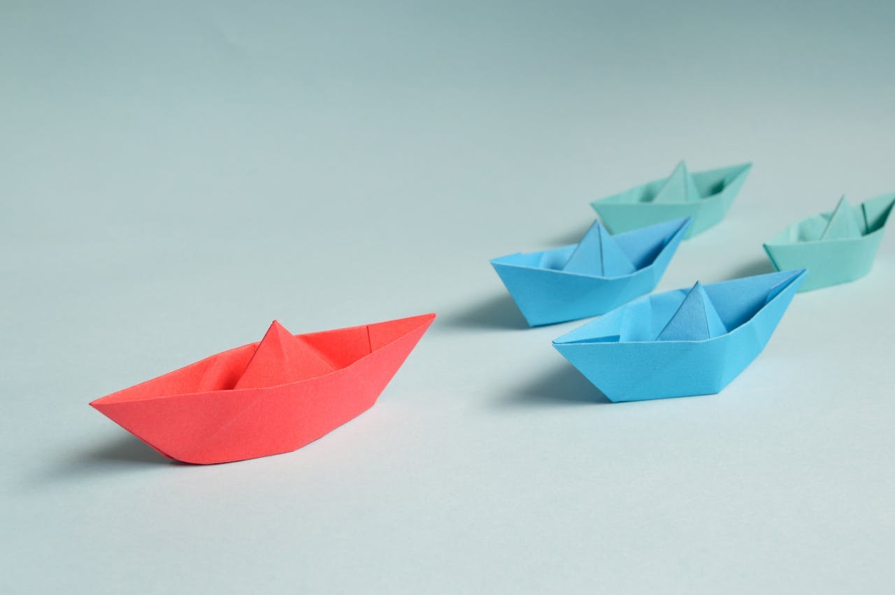 Colorful paper boats with a red boat leading the way