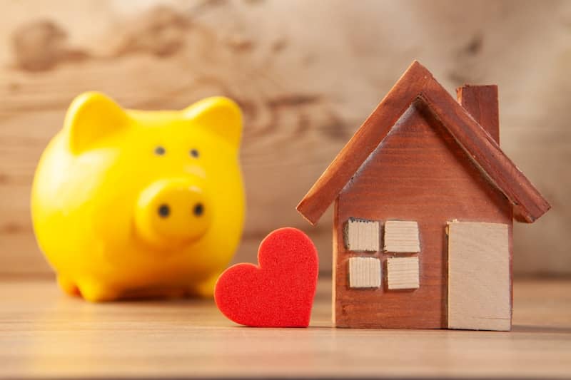 Yellow piggy bank with wooden house and red heart