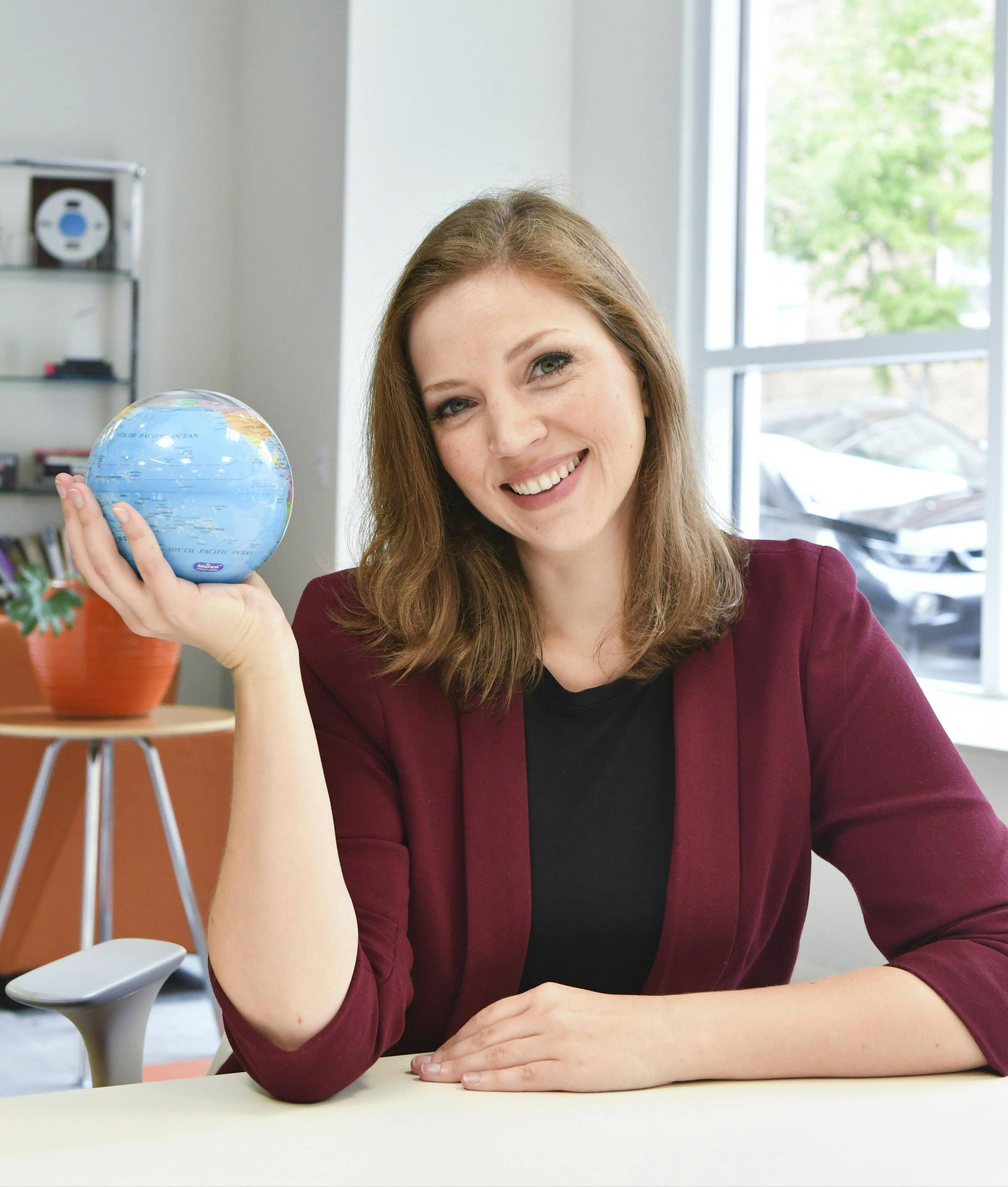 A photo of Amber Melanie Smith holding a globe and smiling.