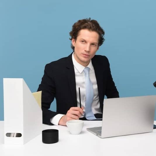 man sitting on chair beside laptop computer and teacup