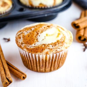a single pumpkin cheesecake swirl muffin in front of a muffin tin
