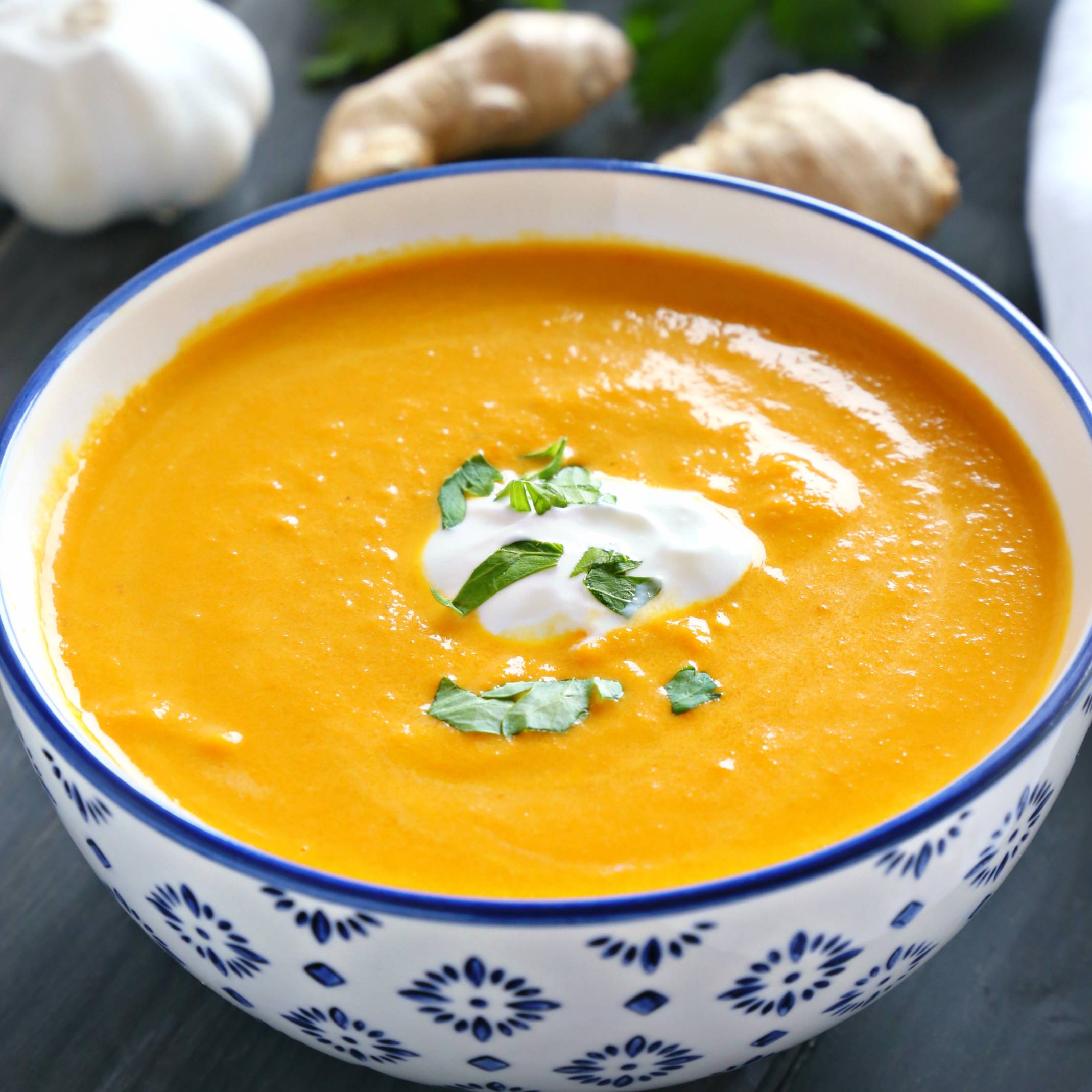 bowl of carrot ginger soup topped with cream and fresh herbs