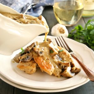 chicken breasts on a plate with white wine mushroom sauce being poured on top