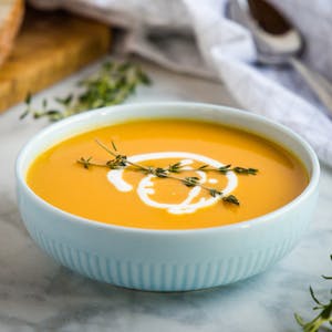 bowl of one pot butternut squash soup with a drizzle of coconut cream and topped with a spring of thyme