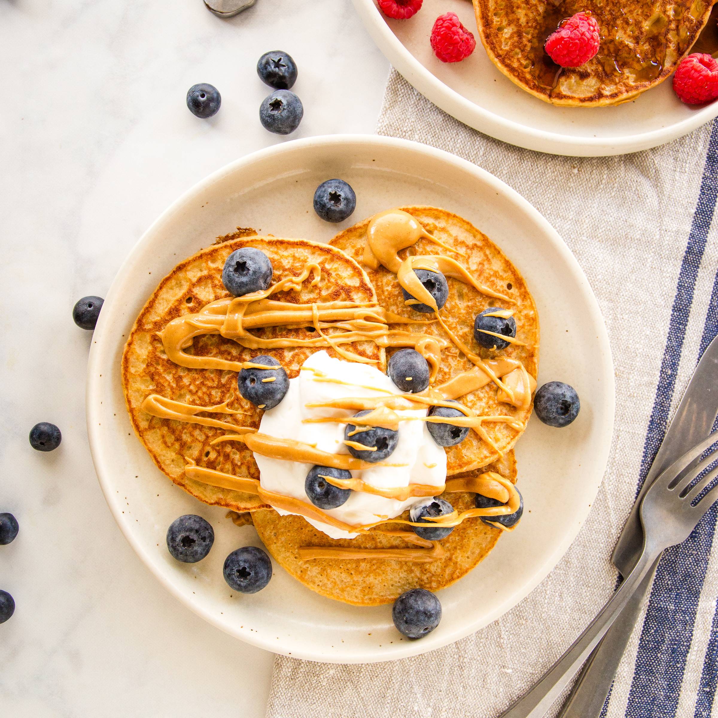protein pancakes topped with greek yogurt, blueberries, and drizzled with peanut butter