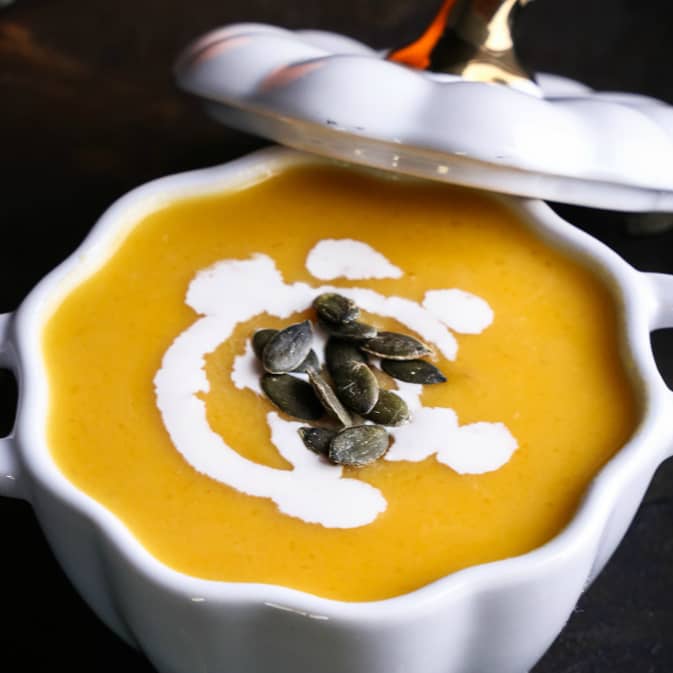 pumpkin soup topped with a swirl of cream and pumpkin seeds