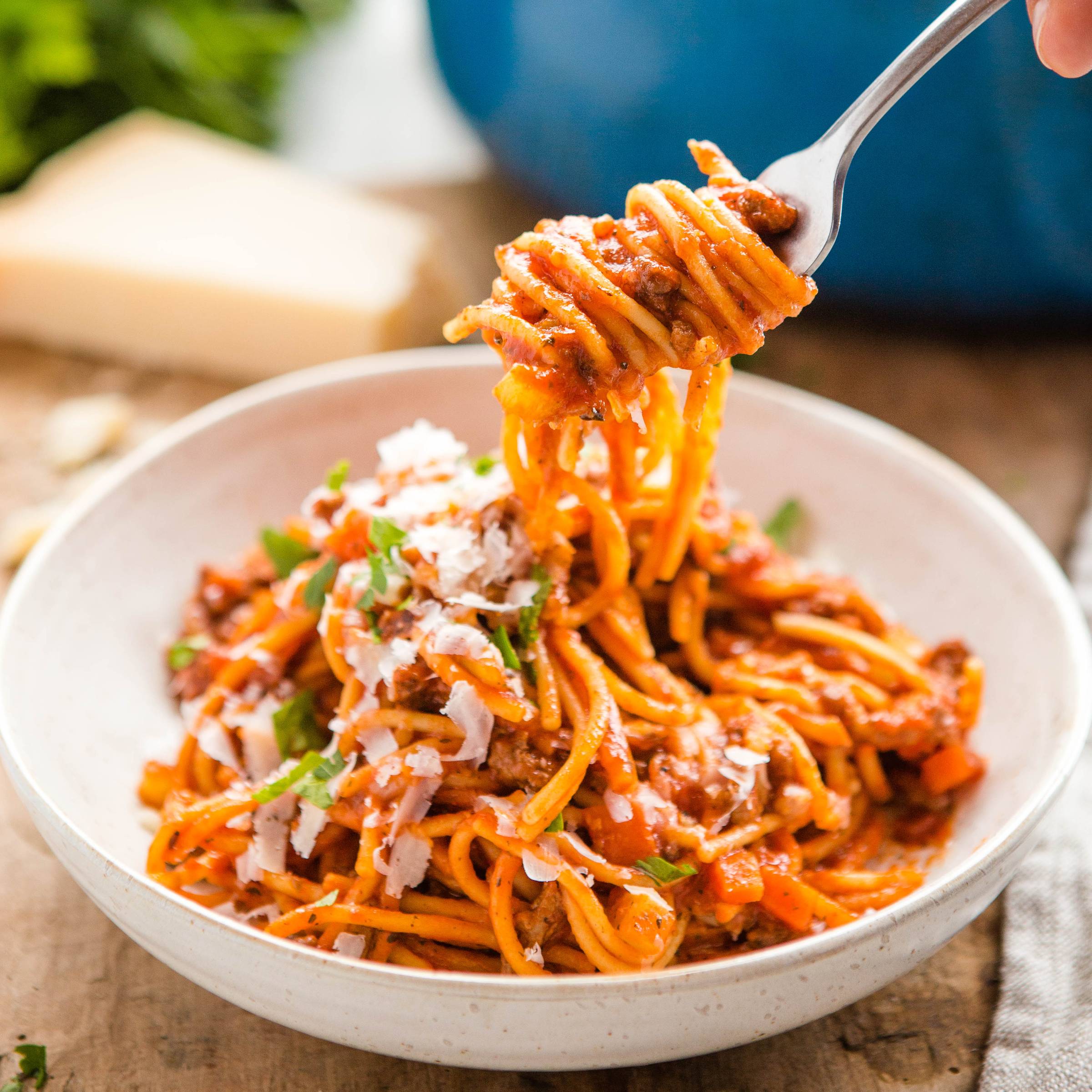 fork with twirled spaghetti above a bowl of spaghetti and meat sauce