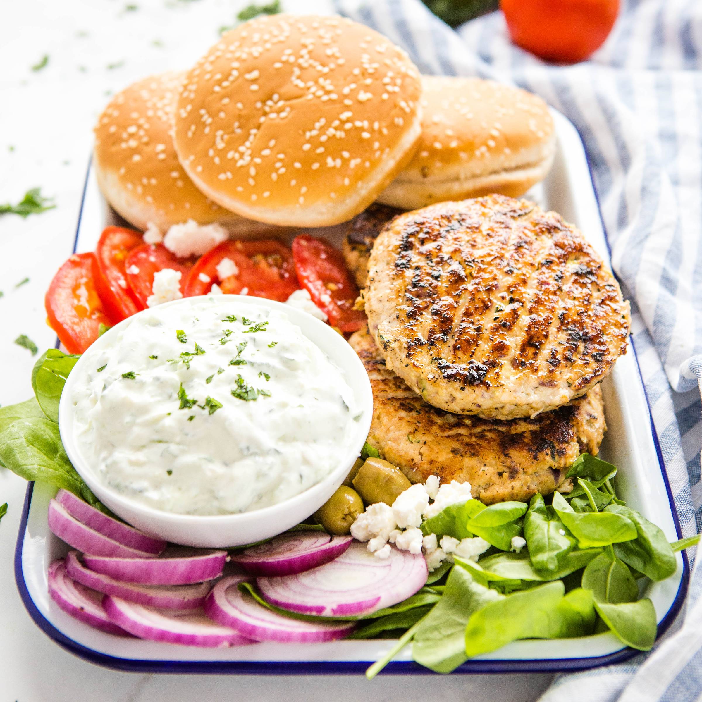 turkey burgers on a platter with tzatziki, buns, and veggie toppings