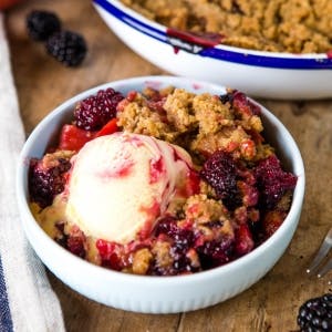 a bowl of apple blackberry crumble with a scoop of vanilla ice cream on top