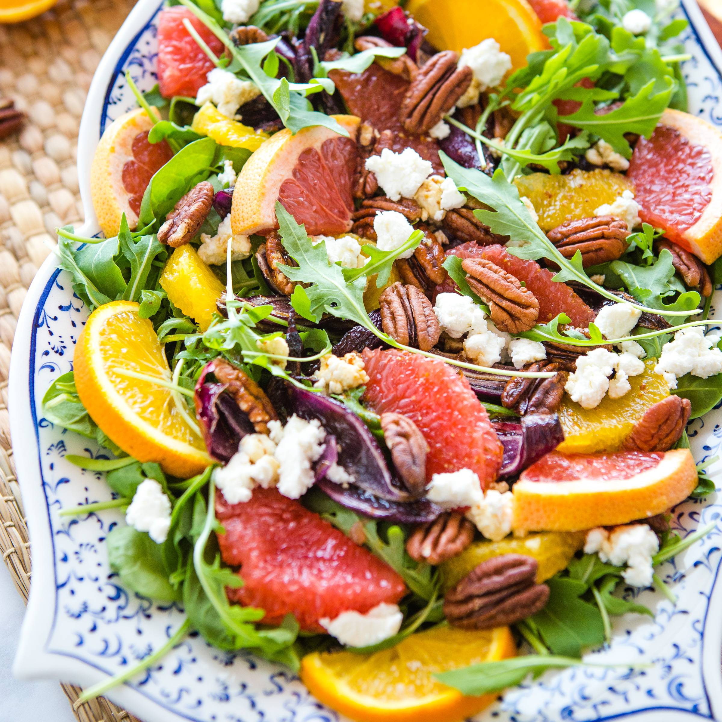 a mixed green salad with citrus segments, pecans, and goat cheese in a porcelain serving dish