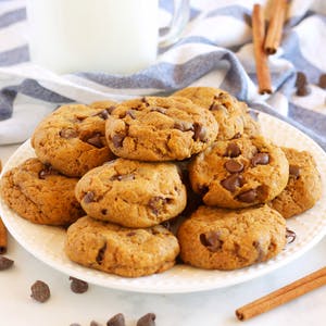 A plate full of pumpkin spice chocolate chip cookies with a glass of milk in the background