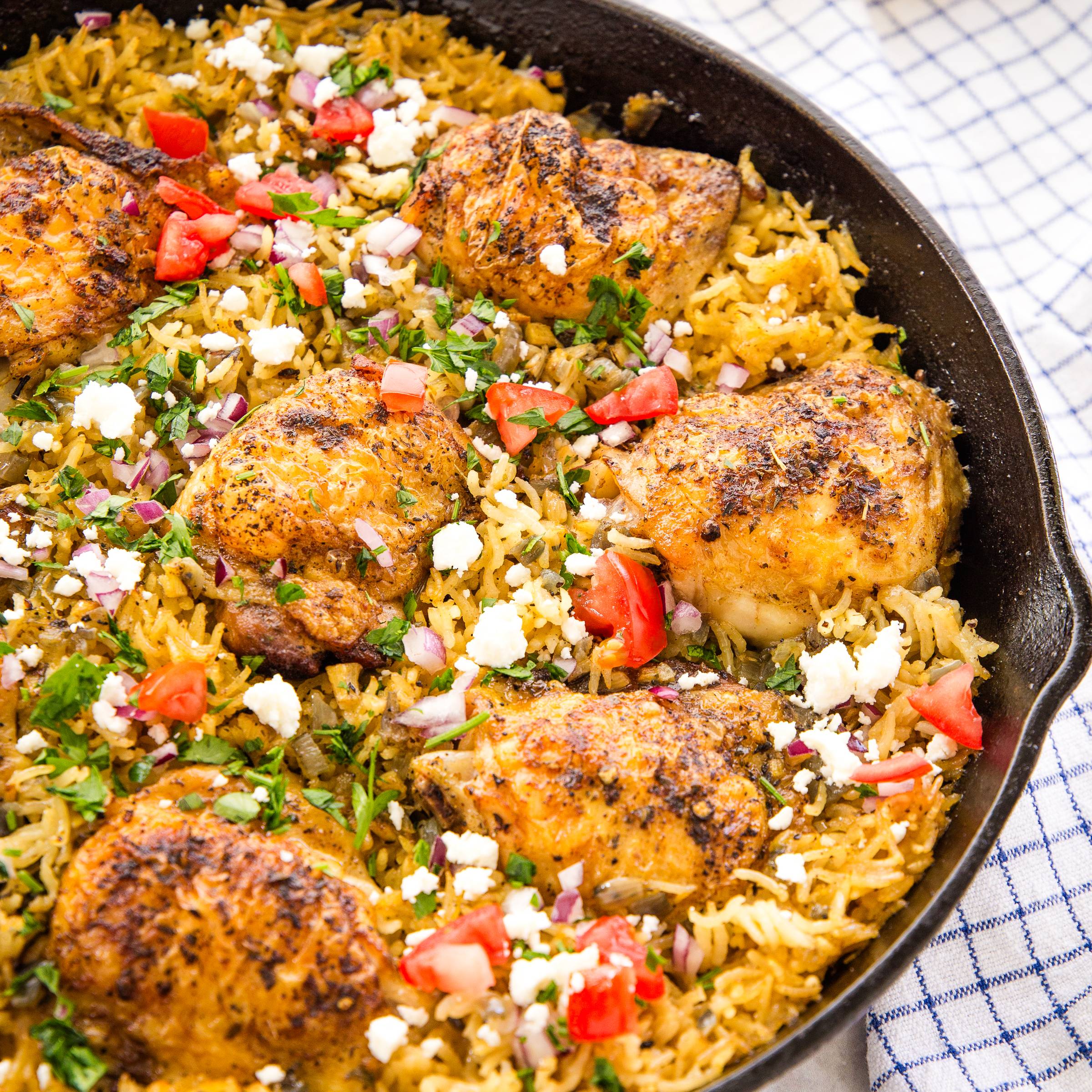 chicken and rice in a cast iron pan topped with fresh herbs and feta cheese