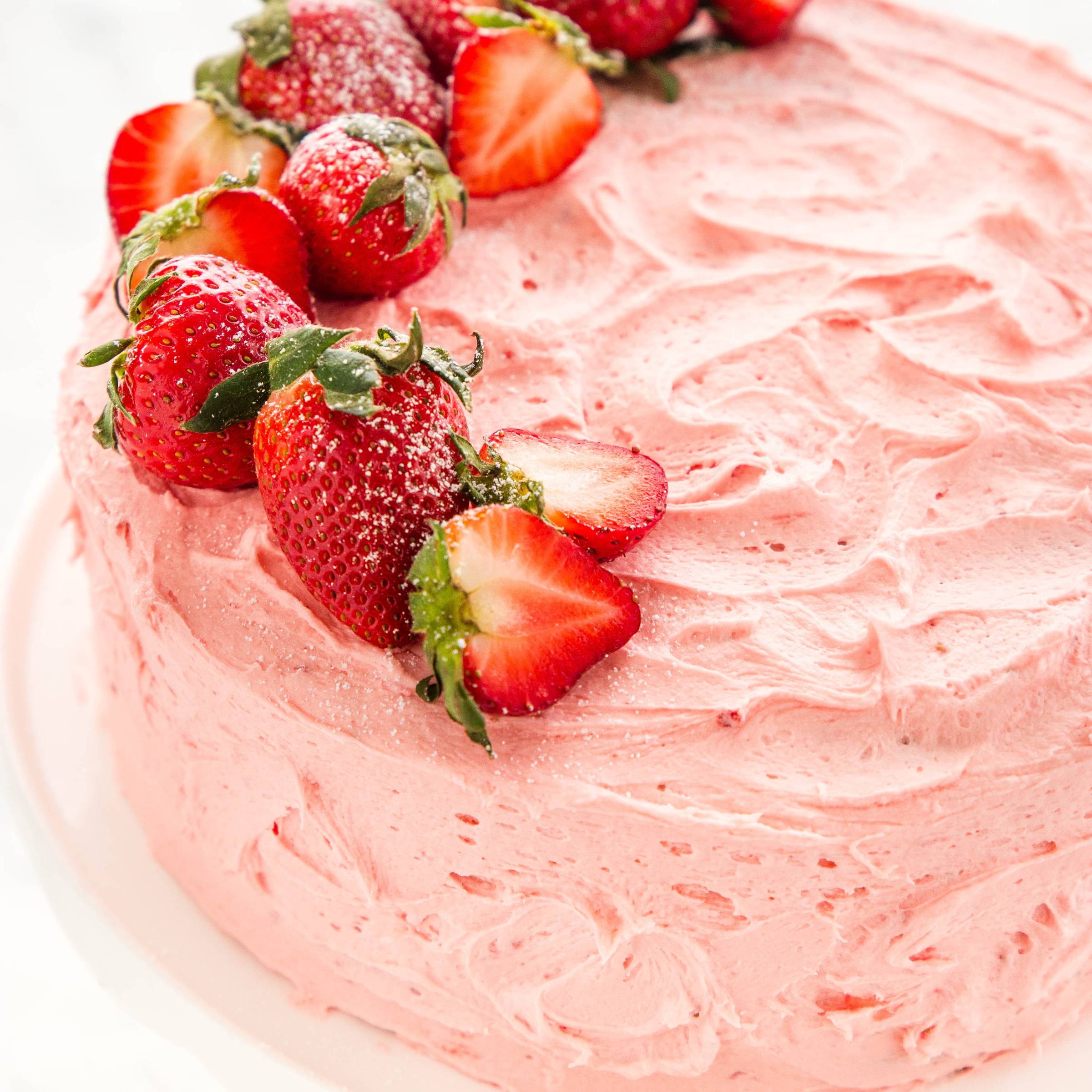 strawberry cake with pink frosting and fresh strawberries on top
