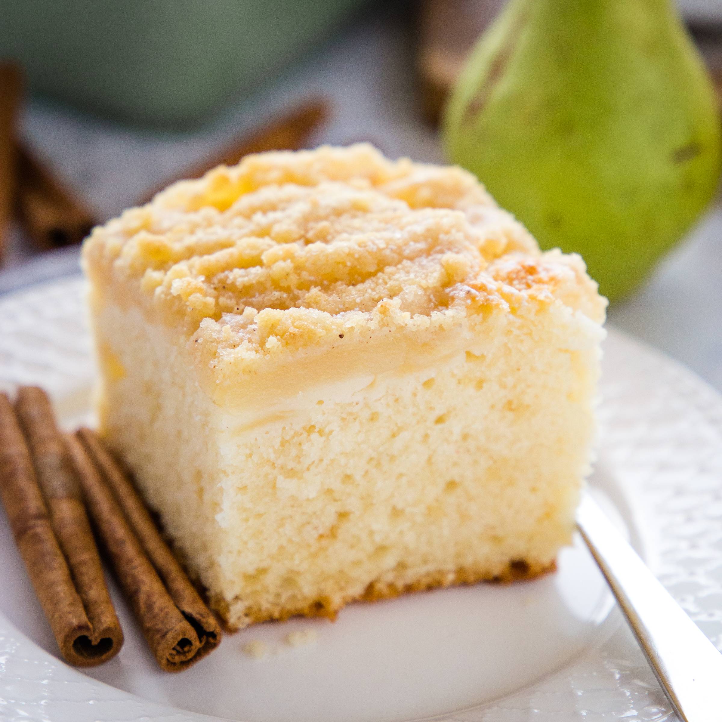 a slice of pear streusel cake on a plate alongside cinnamon sticks