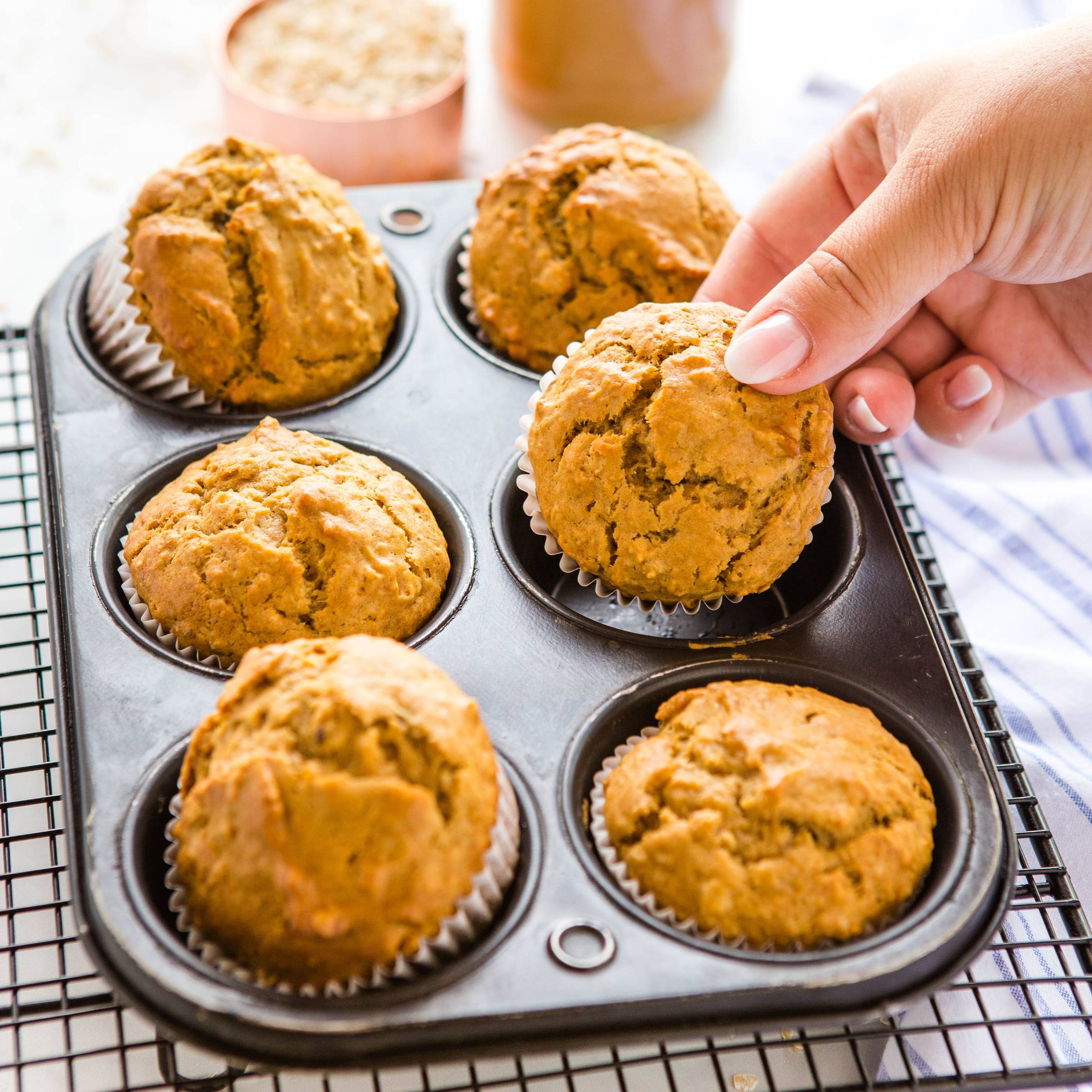 someone removing a peanut butter banana oat muffin from a muffin tin