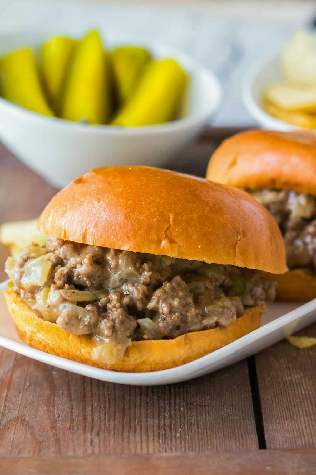 Philly cheesestake sloppy joes on brioche buns with pickle spears in background.