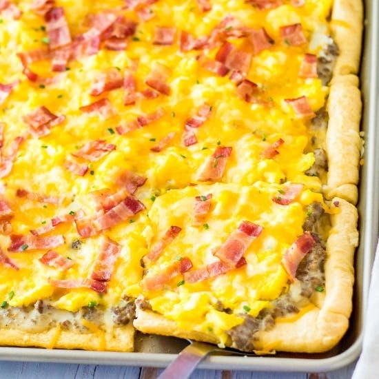 Sheet pan breakfast pizza with crescent roll crust, sausage gravy, eggs, and bacon.