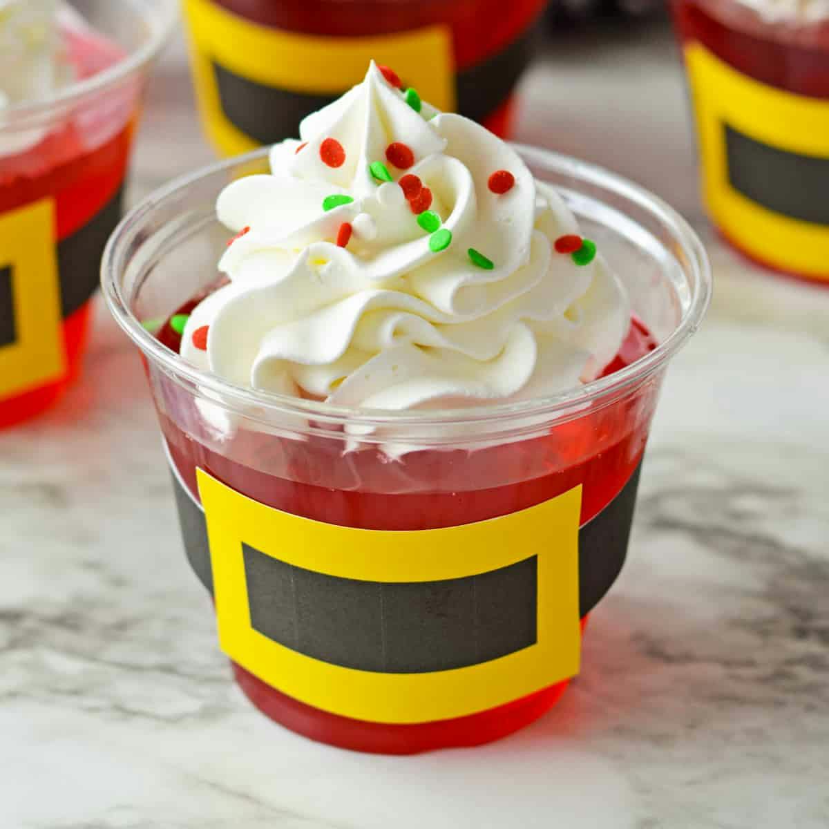 Jello cups topped with whipped cream and decorated to look like santa.