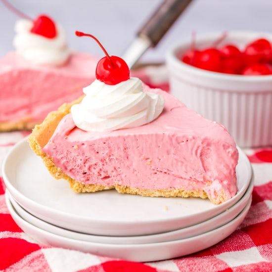 Creamy pink pie slice with cherry and whipped cream on top.