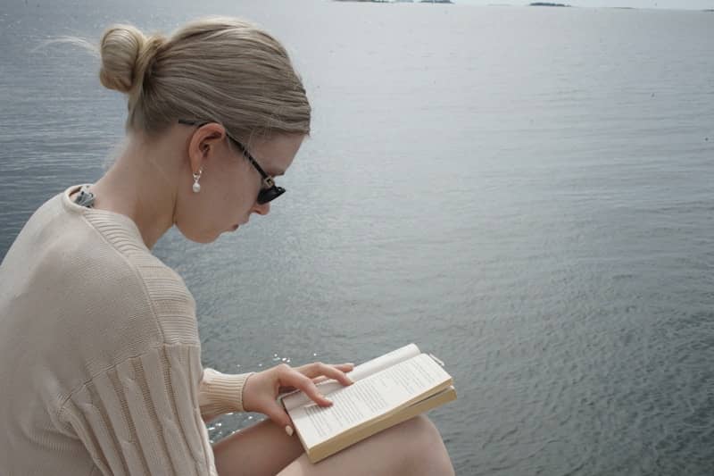 A woman reads a book by the water.