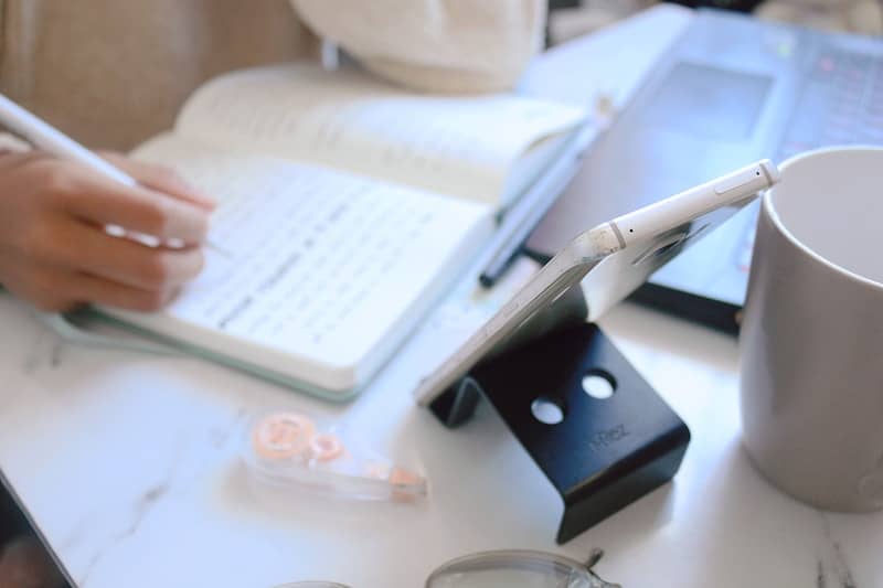 Hand writing in a notebook on a white desk.
