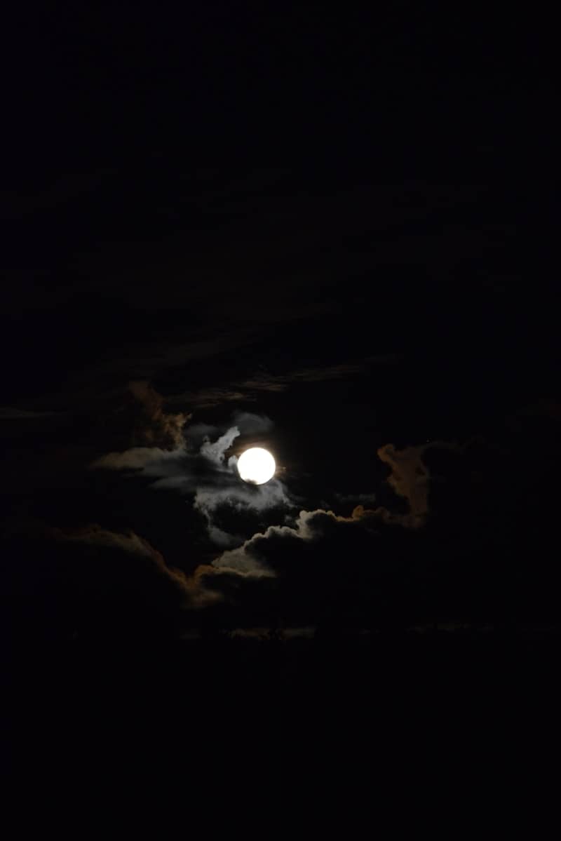 The moon shines brightly through the dark clouds.