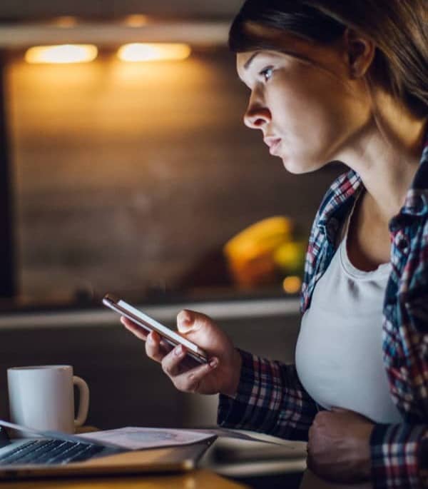 Scene of a mom up late holding her stomach while working on the computer and using her cell phone.