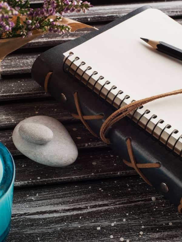 Black leather bound book with journal sitting on a wooden picnic table.