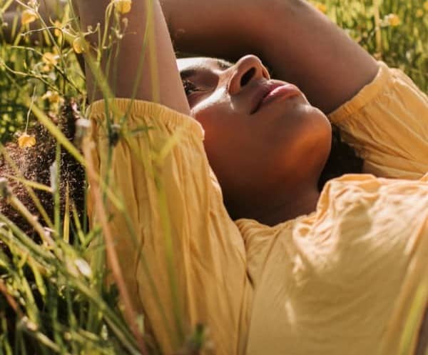 Woman laying in green pasture full of yellow flowers.