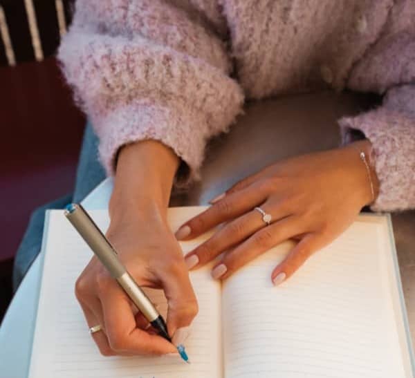 Woman with a pink sweater writing in a journal. 