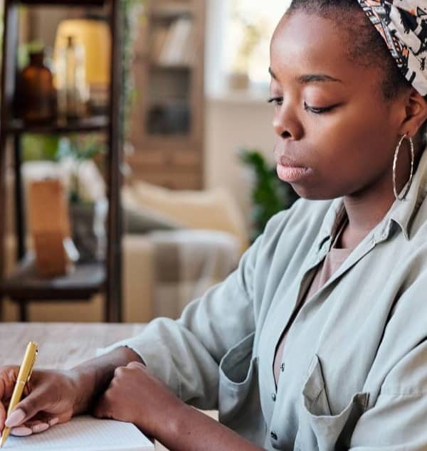 An African American woman sitting in living room writing in a journal.