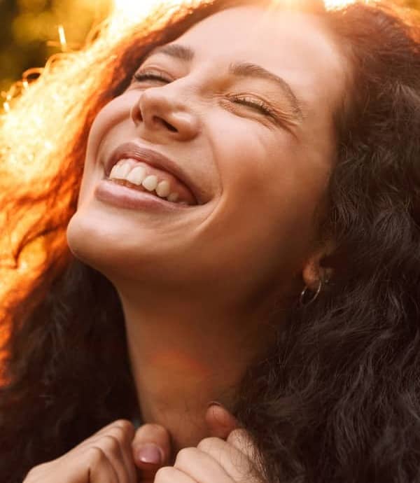 Woman smiling with eyes closed and sun shining in her face.