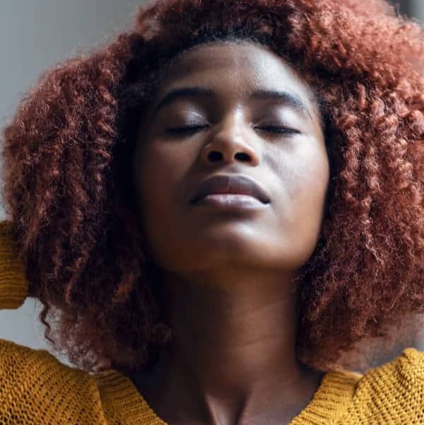 African American woman with hands behind her head with head lifted and eyes closed.