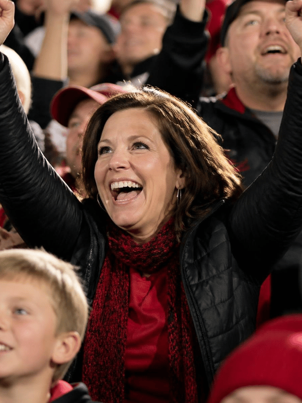 Mom wearing red and black winter clothes cheering the the football stands.