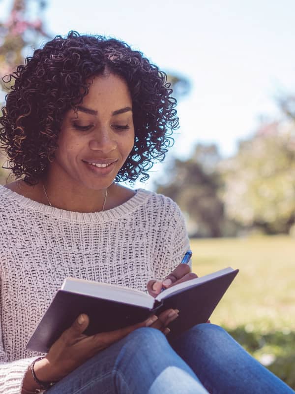 Woman sitting outside in the grass writing in a journal