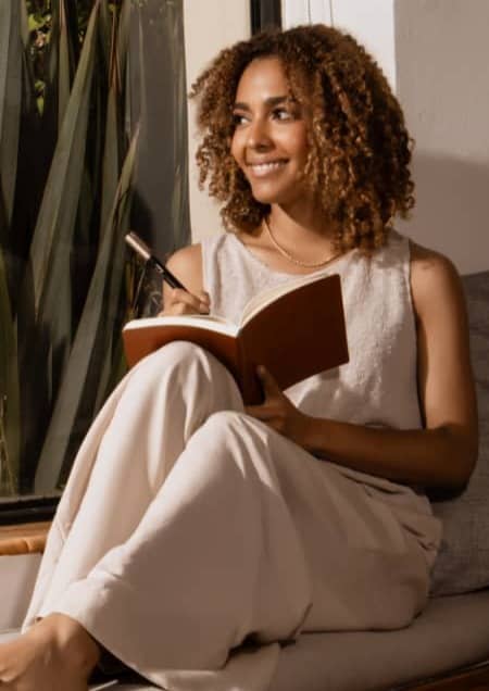 Woman sitting near the window smiling and writing in journal.