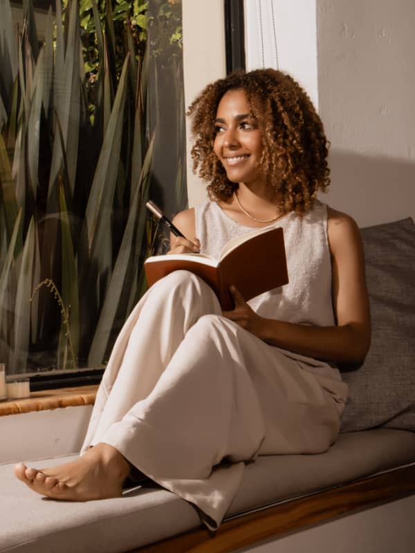 Woman sitting at the window smiling and writing in her journal.